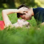 una pareja tirada en el pasto en posicion amorosa juntan sus caras