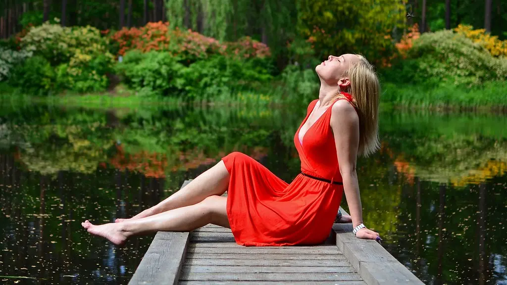 una mujer con vestido rojo está muy relajada en un pequeño muelle donde respira con los ojos cerrados y es feliz