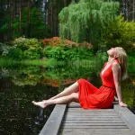 una mujer con vestido rojo está muy relajada en un pequeño muelle donde respira con los ojos cerrados y es feliz