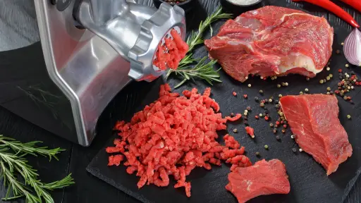 Carne cruda de res dispuesta sobre una mesaa al lado de una moledora de carne