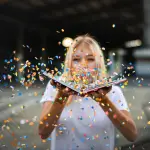 Mujer rubia sopla papel picado de colores desde un libro abierto